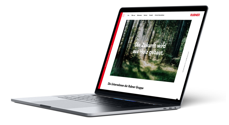 Ein schlanker, offener Laptop zeigt eine Website mit einem Waldbild und dem deutschen Text Die Zukunft wird aus Holz gebaut. Die Website mit dem Schwerpunkt Wohnen und Bauen hat einen weißen Hintergrund mit roten Akzenten und das RUBNER-Logo in der oberen rechten Ecke. Die Gärtner im Allgäu