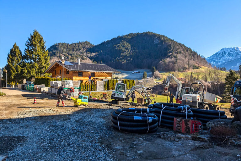 Baustelle mit Baumaschinen und einem Haus und Bergen im Hintergrund. Die Gärtner im Allgäu