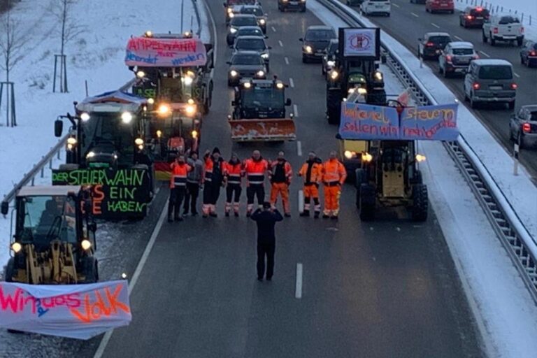 Eine Gruppe von Arbeitern in orangefarbenen Uniformen blockiert eine verschneite Autobahn mit Traktoren, hält Protestbanner hoch und hält den Verkehr auf. Hinter ihnen reihen sich Autos aneinander, und an den Fahrzeugen hängen Transparente mit deutschen Texten. Die Gärtner im Allgäu
